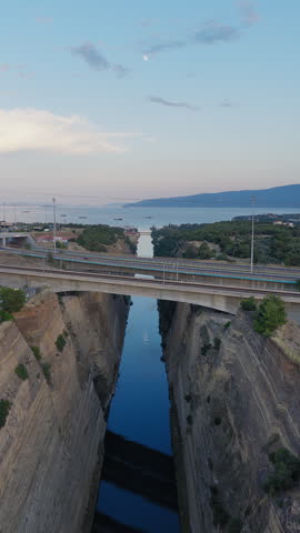 Vertical aerial of Corinth Canal crossing the Isthmus of Corinth at sunset in Greece, drone pullback establishing as cars cross road