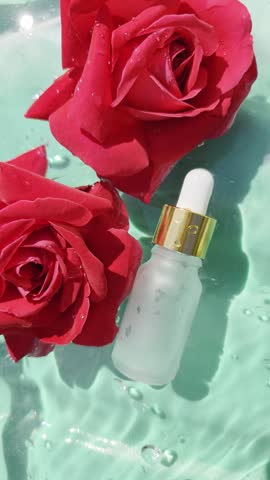 Cosmetic glasses pipette bottle mockup and red roses flowers on water surface with drops. Vertical video. Women