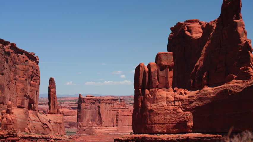 Towering red sandstone formations and dramatic rock spires rise majestically against a vivid blue sky with scattered white clouds in the stunning desert landscape of Arches National Park Utah.