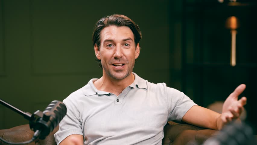 Confident man recording a podcast in a professional studio. The charismatic host is speaking into a microphone during a live interview