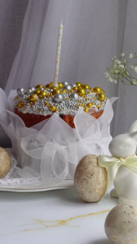 Elegant Easter celebration dessert decorated with golden and silver sugar pearls, a candle, pastel ribbon, speckled eggs, white bunny figurine, and blossoms