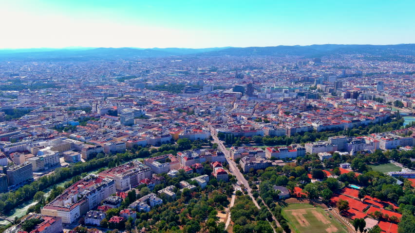 Aerial panoramic drone view of the Vienna cityscape with the Danube Canal, St Stephens Cathedral, rooftops, parks and clay tennis courts, Austria, in summer.