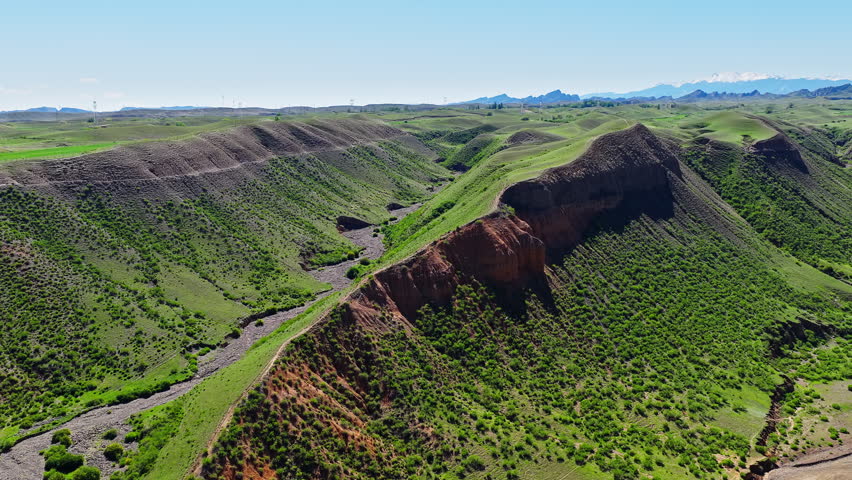 Aerial view of a dramatic mountain ridge with green grass and eroded red soil along the S101 highway in Xinjiang, China