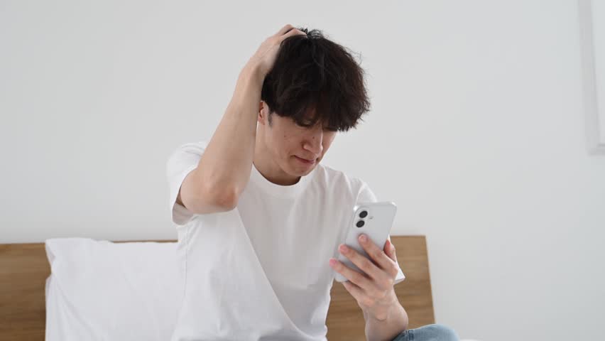 Japanese Man in His Thirties Looking Worried While Using a Smartphone