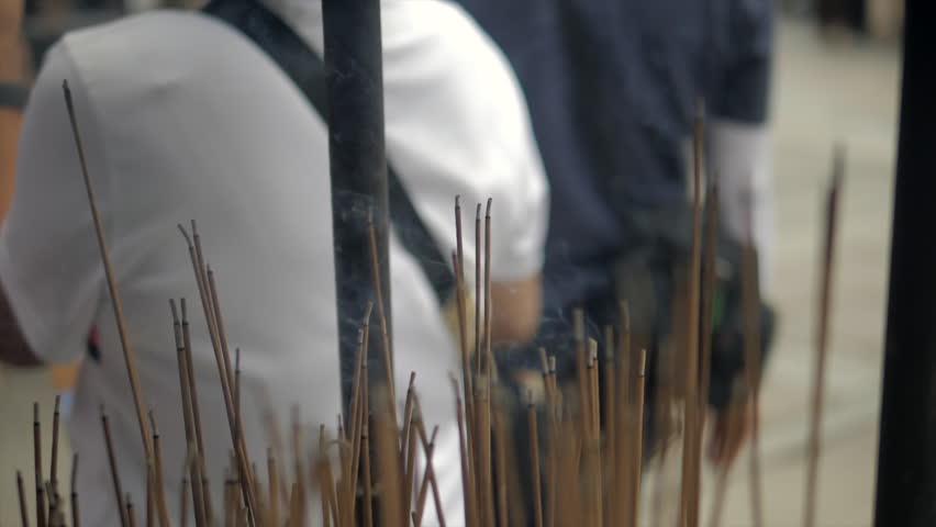 Burning incense sticks in a pot with people passing by at an outdoor Kyoto site