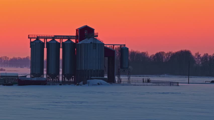 Aerial view of a grain silo standing in a snow-covered field during a vibrant sunset in Europe.