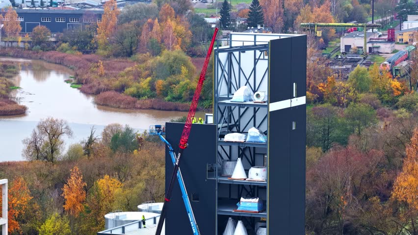 Aerial view of construction site with crane and tall dark structure near river during autumn.