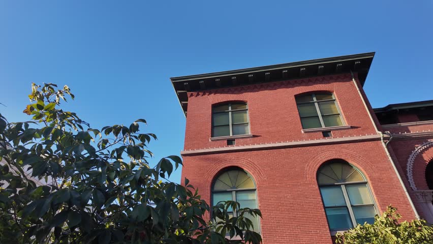 Panning shot of the Alameda City Hall facade, an historic government building in California, showcasing its red brick architecture against a clear blue sky on a sunny day