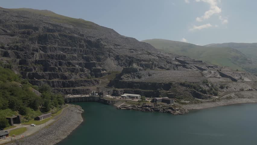 Smooth drone flyover across Llyn Padarn showcasing tranquil waters, forested shores, and the towering mountains of Snowdonia National Park. drone moving to the right over the lake.