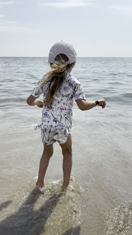 Young girl joyfully jumping in the sea at Dziwnówek, Poland, during a sunny summer day. The video captures a carefree childhood moment by the Baltic Sea, with waves, water, and a relaxed holiday atmosphere.