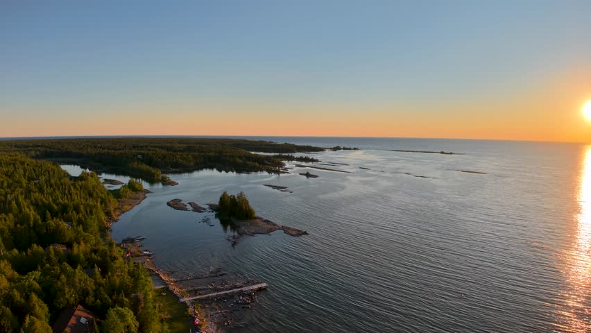 Setting sun shines across open Lake Huron beside a rugged forested Tobermory coastline