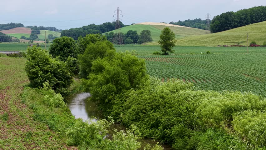 A winding country road curves between lush farm fields and trees in rural eastern Ohio