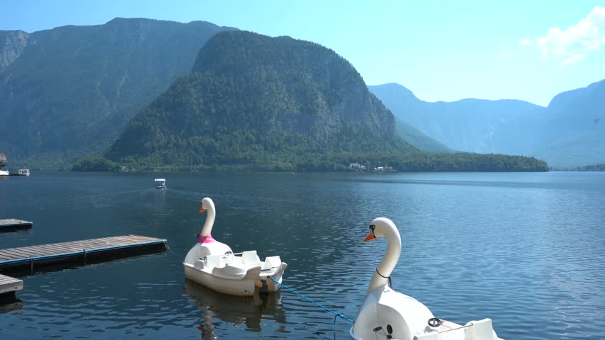 Swan Pedal Boats Floating on Hallstatt Lake with Alpine Mountains in Background in Austria.