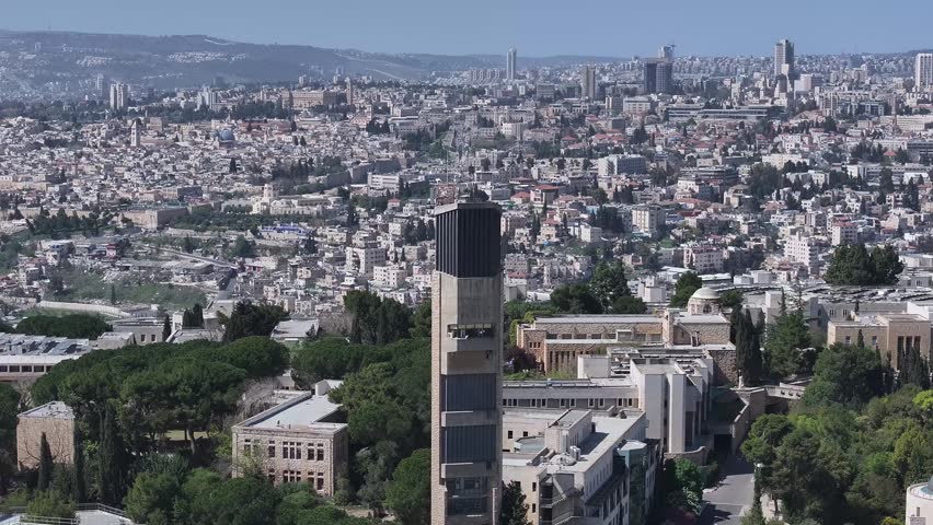 High angle aerial shot revealing the Mount Scopus campus bell tower with the sprawling Jerusalem urban landscape and Old City landmarks in the background.