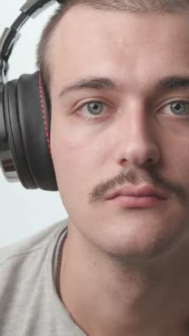 Close-up of a young man wearing headphones, looking shocked with open mouth, then raising his hands and cheering with excitement against a white background.