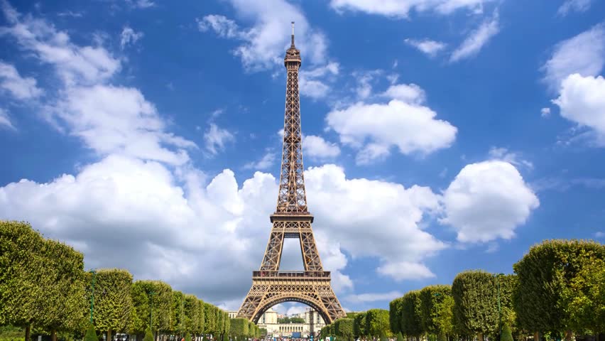 Breathtaking view of Iconic Eiffel tower architecture framed by park trees in Paris, France. The historic iron lattice monument stands tall against a vibrant blue sky.