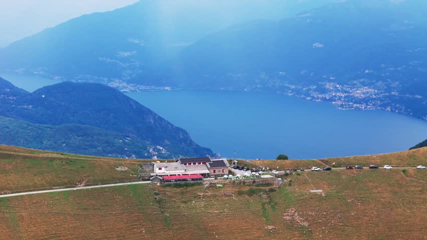 Majestic aerial view of a mountain refuge nestled on a grassy ridge, offering a breathtaking panorama of a stunning blue lake in the alps