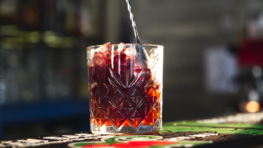 Bartender pouring clear liquid into a red iced drink in a crystal glass at a bar