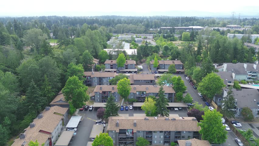 Clustered multi story apartment buildings line Pete von Reichbauer Way South, featuring dark roofing interspersed with bright foliage, reflecting regional architectural designs in Federal Way, WA. USA