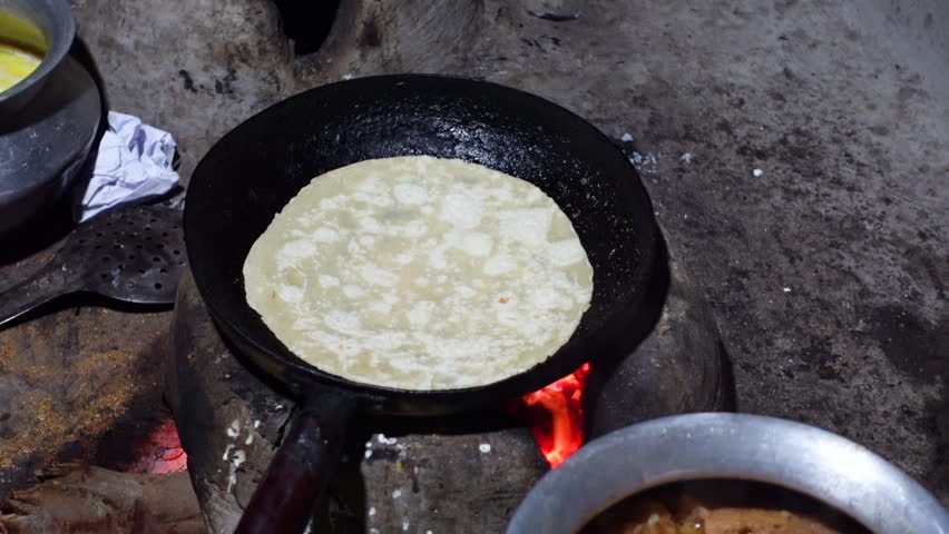 Bread being baked in a fry-pan in a clay oven.