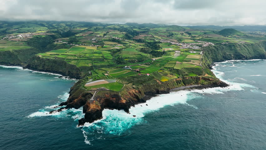 Aerial view of a rural peninsula with patchwork farmland, Atlantic Ocean on both sides. Agricultural coastal landscape of Sao Miguel Island