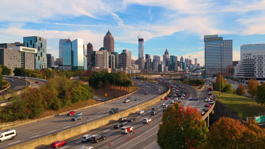 Rush hour highway traffic driving past Atlanta city landscape with tall skyscraper buildings. Fast urban rhythm, daily commute and metropolitan lifestyle.