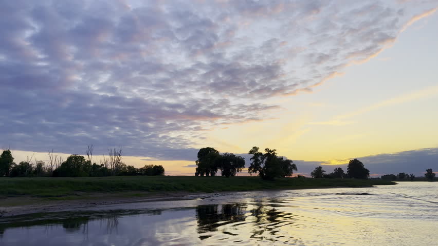 Tracking shot from a moving boat shows a golden sunset against an interesting cloud formation on the Elbe River in Germany.
