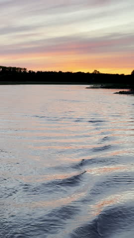 Vertical video tracking shot from a moving boat shows a pretty orange sunset over the Elbe River in Germany. 