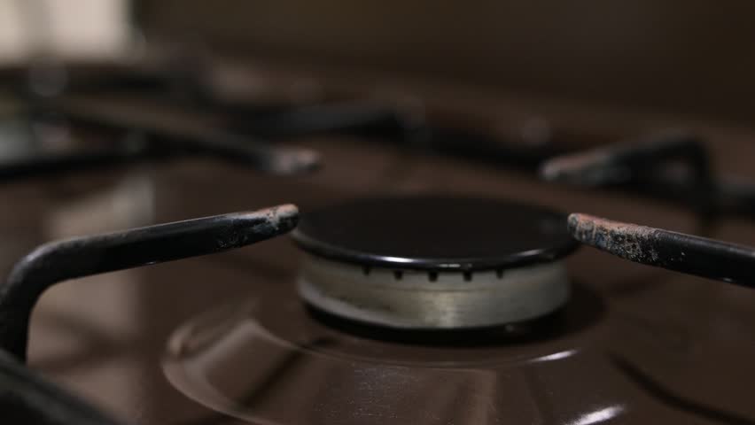 A person lighting a gas stove and putting a metal pot on it. A male hand turns on a burner, then a saucepan is placed on the blue flame for cooking or boiling water