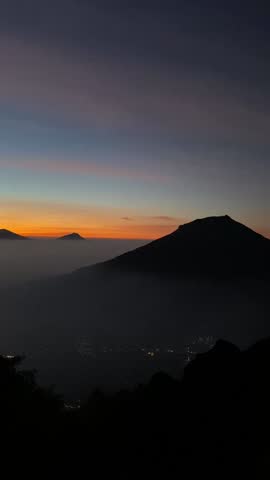 Vertical footage of hikers gathering near a dead tree at a mountain summit during sunrise.