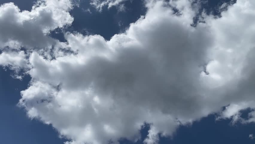 A peaceful view of bright white fluffy clouds moving slowly across a deep blue sky during a sunny day.