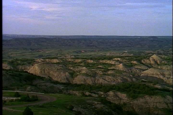 Pan across prairie dotted with hills of sedimentary rock formations and buttes in Medora, North Dakota.