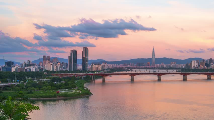 Pink summer sunset glows over Han river as Seongsu bridge and Lotte tower rise against Seoul skyline and mountains