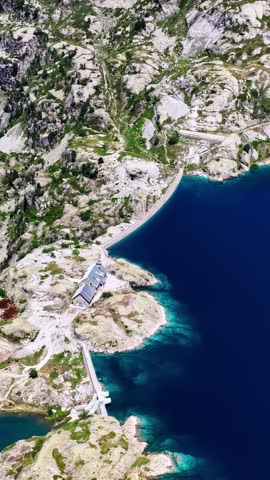 Mountain lake and alpine dam at Artouste in French Pyrenees from above, drone vertical background of building on rocky shoreline