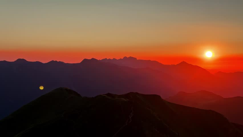 Sunset over mountain ridges with vivid orange sky and distant peaks in silhouette