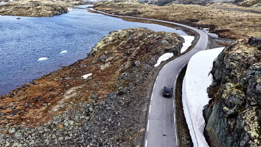 Aerial view of a vehicle traveling on a winding road through a rocky, snowy Norwegian mountain pass