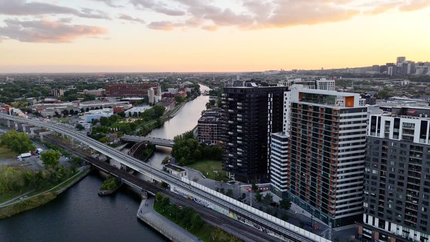 Passenger train passing through Griffintown, Montreal, Quebec, Canada at sunset with modern skyline. g.
