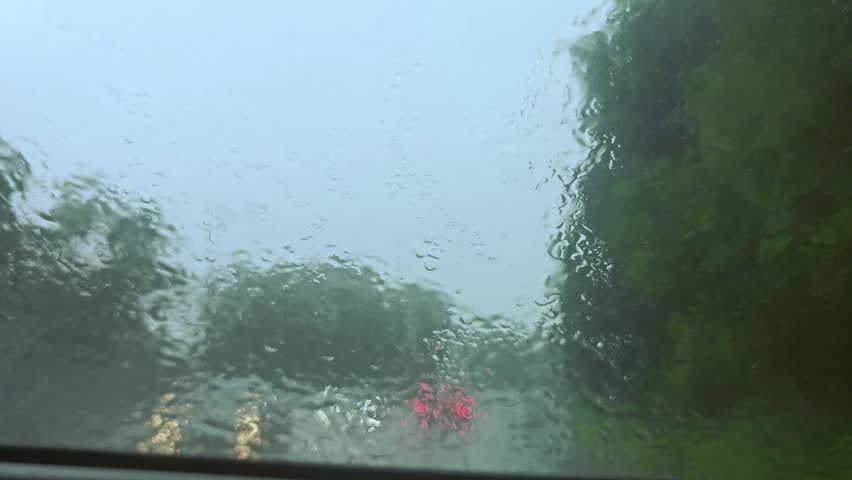 Rain on the windshield as the car drives through the city, heading towards oncoming vehicles with their headlights on.