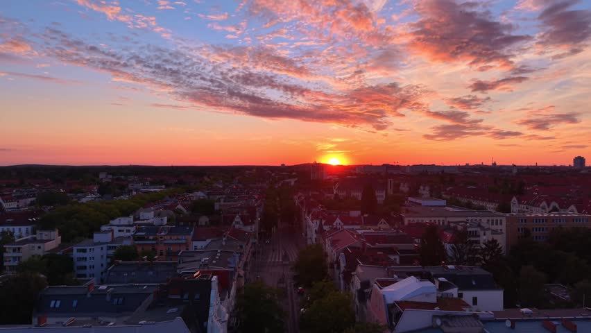 Berlin city showing buildings and trees under a vibrant orange and yellow sunset sky with clouds. Nice aerial view ascending raise up drone panorama