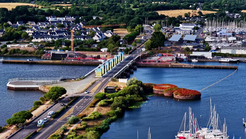 Colorful dam bridge crosses river between marina full of sailboats and village rooftops at Port d Arzal Camoel in Brittany