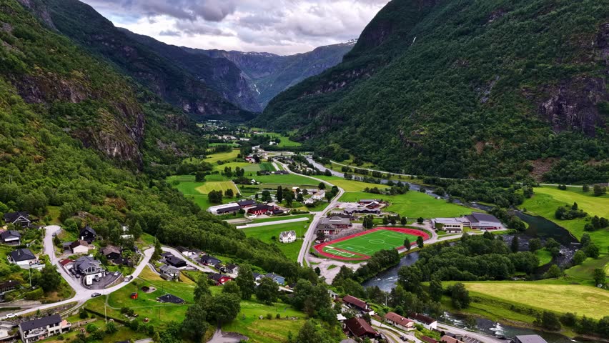 Aerial descent revealing colorful houses and sports field in Aurland mountain village in Norway and Aurlandsdalen valley