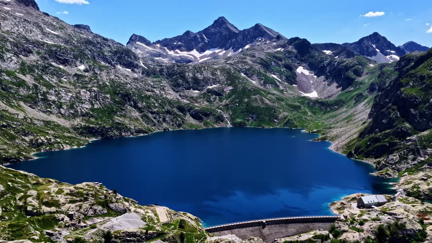 Aerial view of deep blue mountain lake surrounded by rugged peaks and dam structure