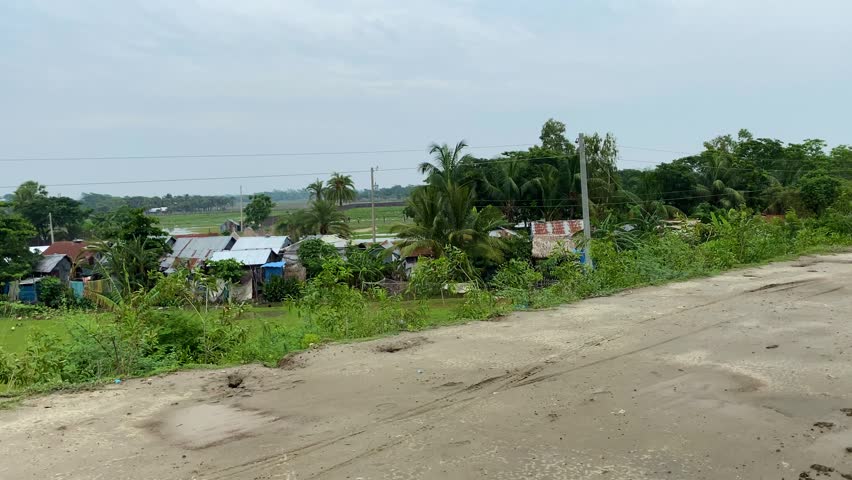 Rural village settlement alongside muddy country road with cloudy sky and trees