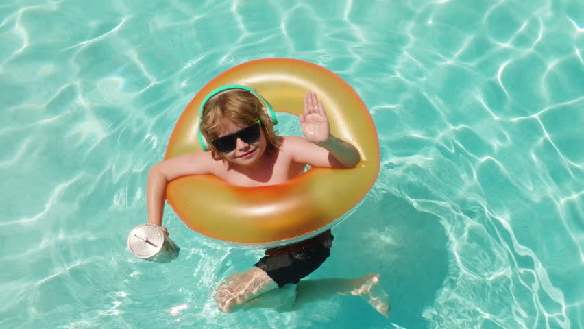 Happy Child Relaxing in Swimming Pool with Inflatable Ring and Headphones. Top view of a happy child floating in a swimming pool with an inflatable swim ring. Kids summer vacation.