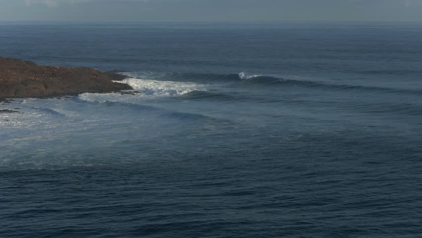 A long shot moving closer to the breaking waves along this beautiful coastline with soft evening lighting.