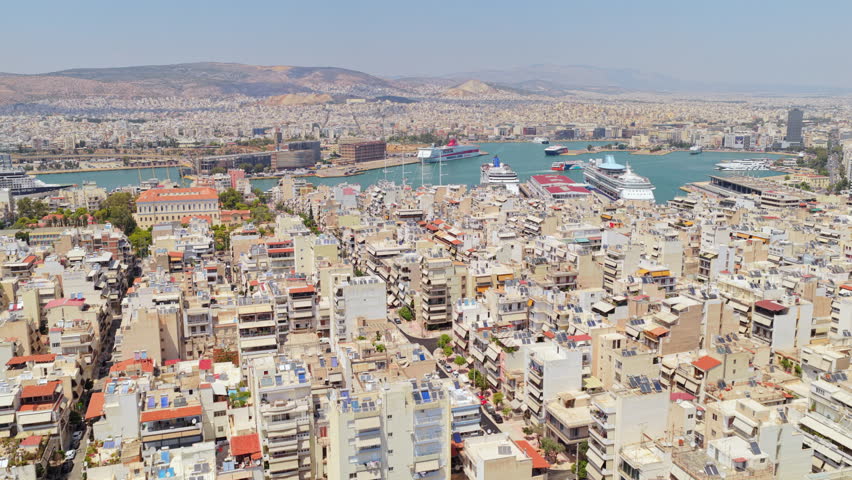 Beautiful aerial establishing shot flying over the dense urban landscape and harbor of piraeus, the historic port of athens, with multiple cruise ships and ferries docked on a sunny summer day