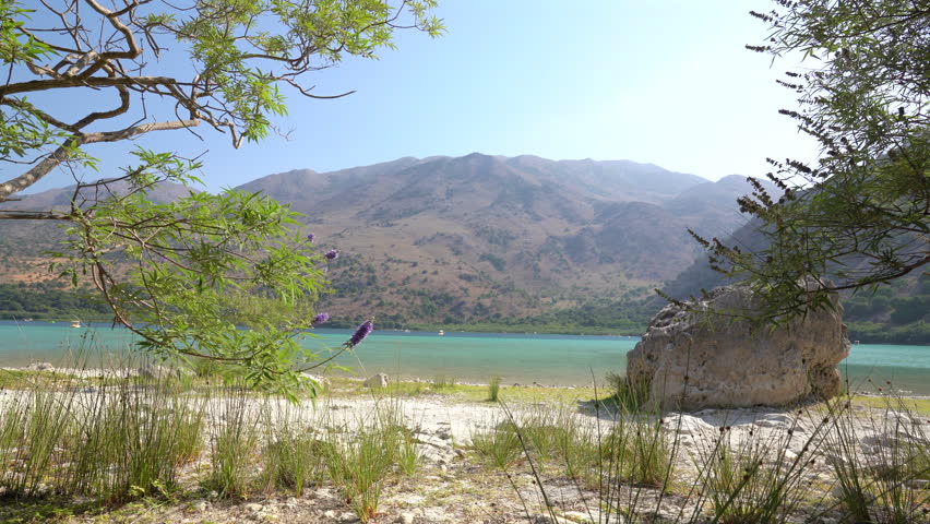 Scenic view of Lake Kournas in Crete, Greece, surrounded by Mediterranean vegetation and mountains on a sunny summer day. Crystal clear freshwater and peaceful natural landscape.