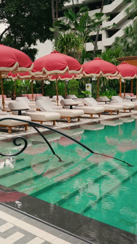 Outdoor swimming pool with luxury sun loungers, tropical gardens and wooden cabana at a modern hotel resort. 4K 60FPS Medium Shot.
