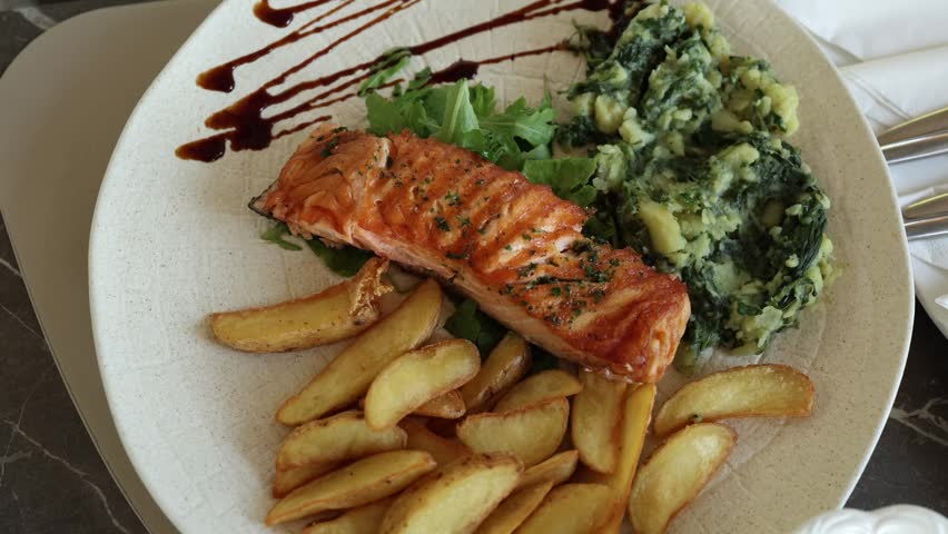 Grilled salmon fillet served with golden potato wedges spinach and fresh greens on a restaurant plate showing a healthy seafood meal during a relaxed summer vacation meal