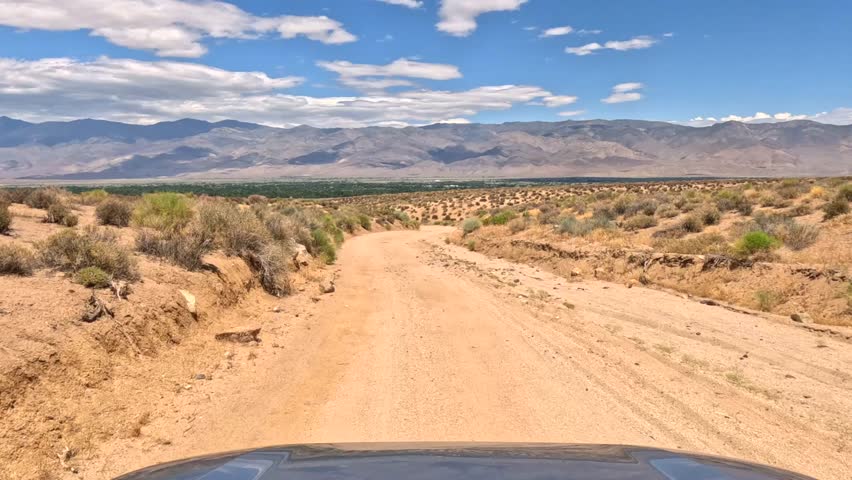 Dirt Road Through Arid Desert Valley Under Blue Sky With Clouds